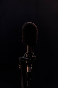 Close-up of a black microphone in a studio setting, isolated on a dark background.