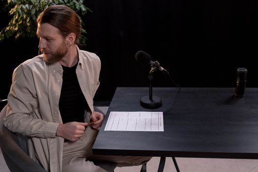 A man sits at a table with a microphone, preparing for a podcast in a studio setup.
