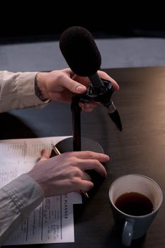 A person adjusts a microphone on a desk surrounded by a mug and planner, perfect for podcasting themes.