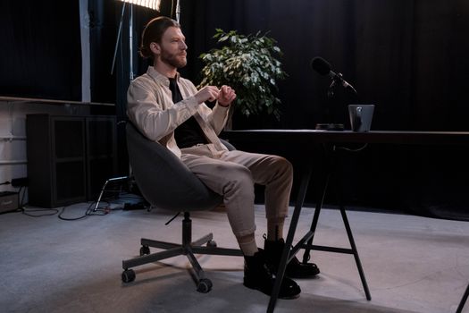 A bearded man sitting in a modern podcast studio with a microphone.