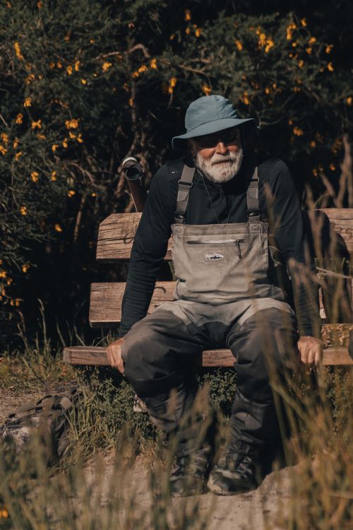 Free Elderly man in overalls and bucket hat sitting on a wooden bench in a sunny park. Stock Photo
