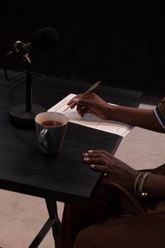 A person recording a podcast with a microphone, cup of tea, and notes on a table.