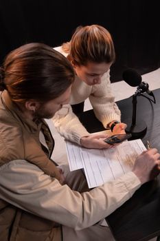 An overhead view of two people reviewing documents using a smartphone and microphone.