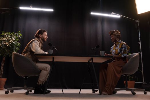 A man and woman recording a podcast in a professionally lit studio with microphones.