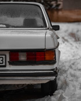 Close-up of a vintage car's tail light covered in snow, showcasing classic design.