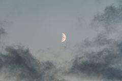 A serene view of the half moon peeking through dramatic clouds in the evening sky.