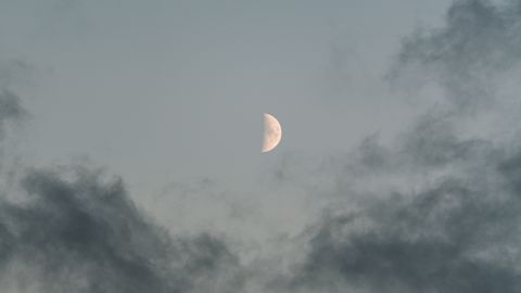 A serene view of the half moon peeking through dramatic clouds in the evening sky.