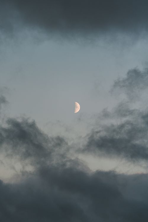 Free A serene view of the half moon peeking through dramatic clouds in the evening sky. Stock Photo