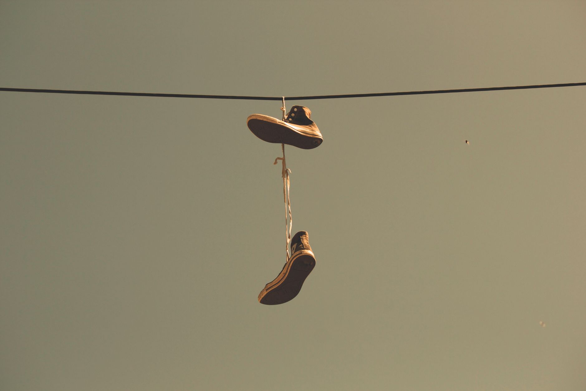 Casual sneakers hanging by their laces on a power line under a clear sky, creating an urban scene.