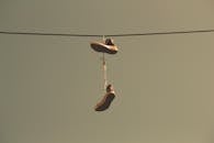 在晴朗的天空下，一双休闲运动鞋用鞋带挂在电线上，营造出城市场景