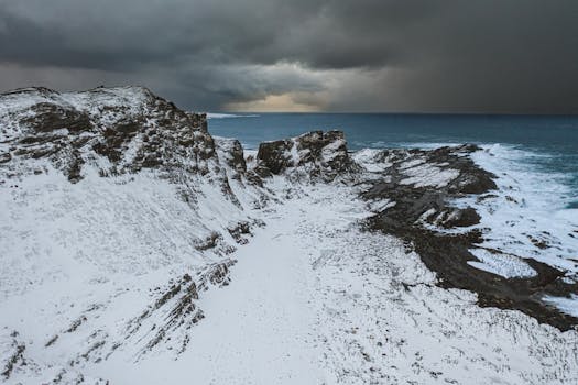 Winter landscape of snow-covered cliffs and sea in Vayda-Guba, Russia under a dramatic sky.