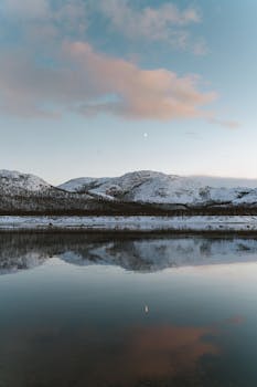 Stunning view of snow-covered mountains reflected in a serene lake at sunset with a clear sky.