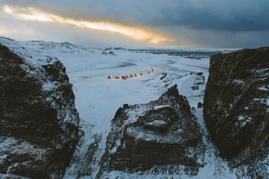 Drone capture of a snowy expanse near Vayda-Guba, Russia, at sunset showcasing rugged winter terrain and dramatic skies.