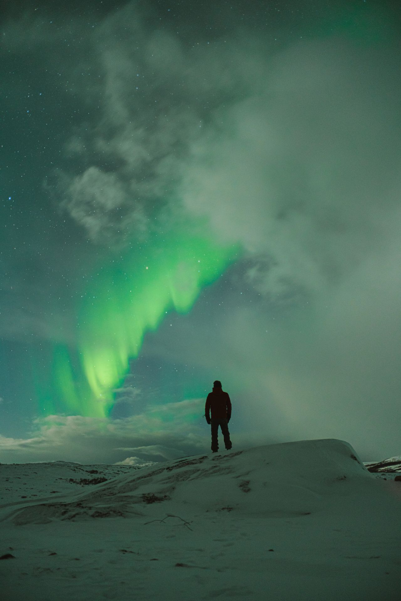Person standing on rocks under the northern lights
