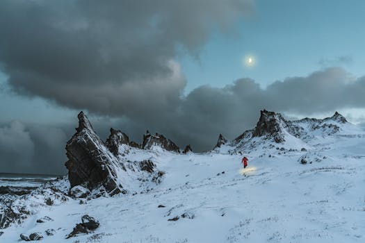 Adventurous hiker traverses snowy mountain terrain under a moody sky.