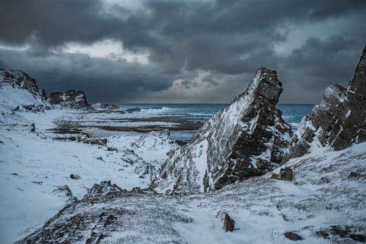 Snow-covered rocky coastline under a cloudy sky, capturing the essence of winter.