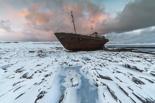 A dramatic shipwreck in a snowy arctic landscape during sunset, captured with a drone.