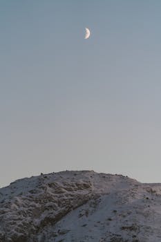 Crescent moon shining above a serene, snow-covered mountain landscape, capturing the tranquility of winter.