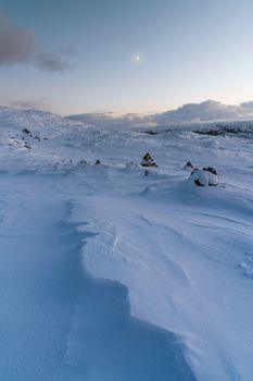 Serene winter landscape with snow and pale sky at dusk, featuring distant mountains.
