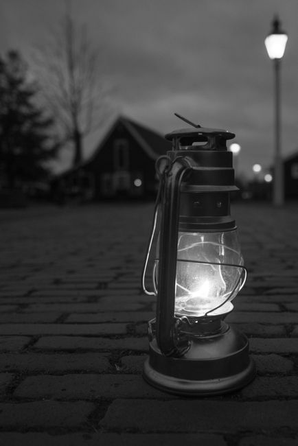 A vintage lantern illuminates a cobblestone street at night, creating a nostalgic urban scene.