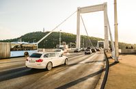 Cars and a bus crossing Erzsébet Bridge with a scenic view of Budapest in the daytime.