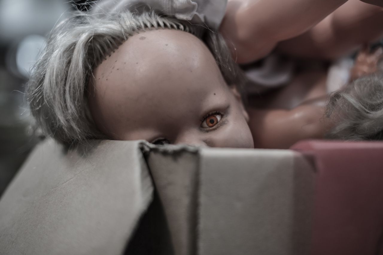 Close-up of an eerie doll half-buried in a cardboard box, evoking mystery and curiosity.