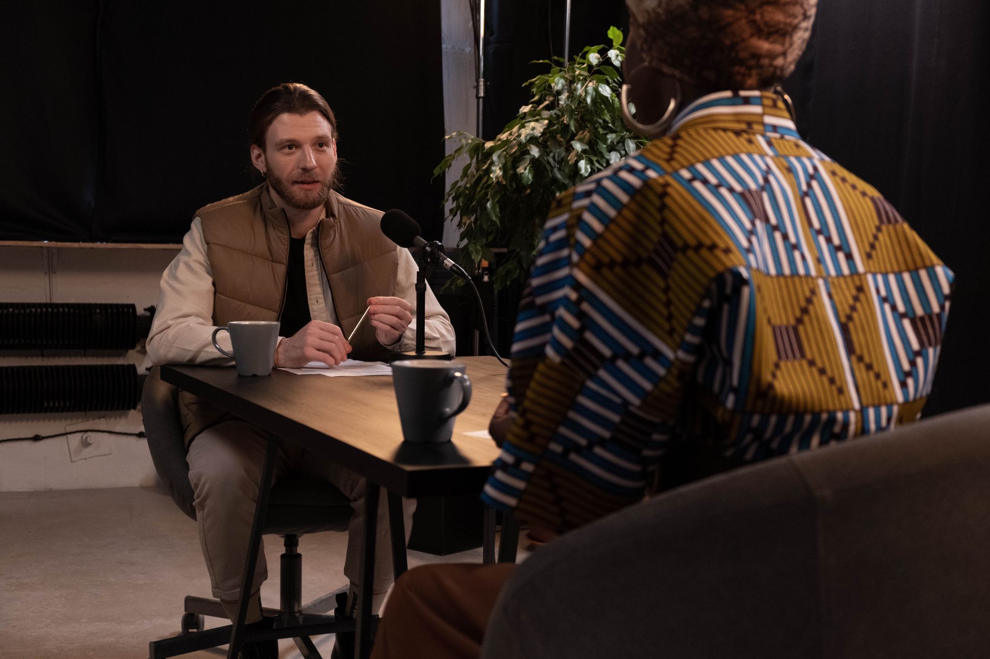 Two hosts talking across a table in a dim recording studio — photo by cottonbro studio on Pexels