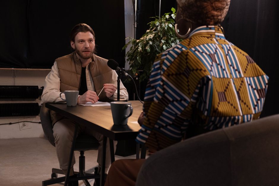 Two people talking across a studio desk with a microphone, photo by cottonbro studio on Pexels