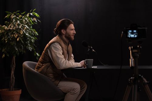 Free A man sits at a table in a studio setting, recording a podcast with a microphone. Stock Photo