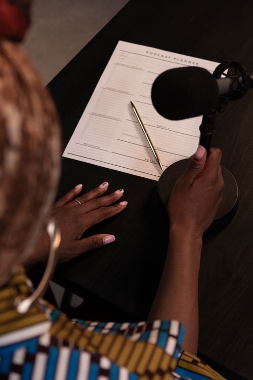 Free An overhead view of a person with a microphone and podcast planner on a desk. Stock Photo