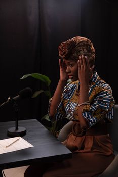 Stylish woman in turban prepares to podcast, adjusting microphone in a studio setting.