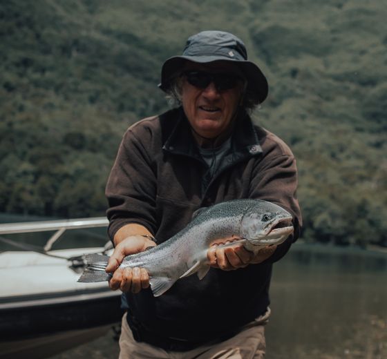 A senior guide proudly holding a rainbow trout beside the boat