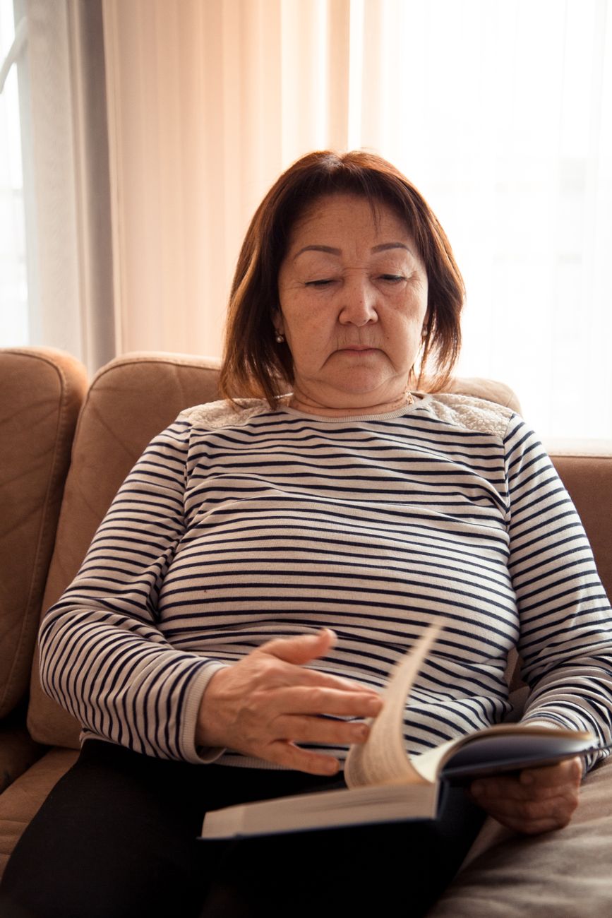 Middle aged ethnic focused female looking through interesting novel on sofa of lounge in daytime
