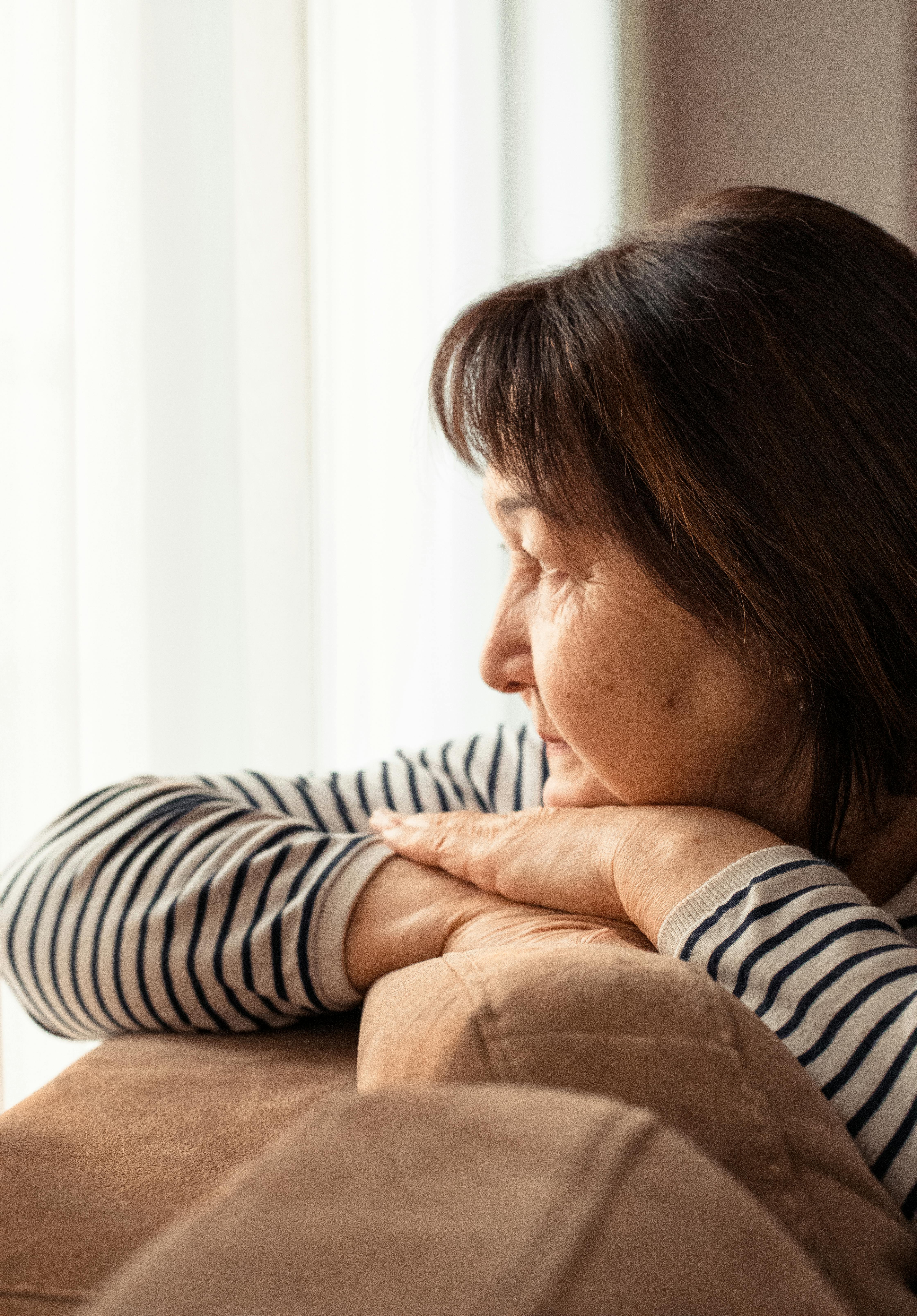 Side view of crop ethnic female with wrinkles looking away in daylight at home