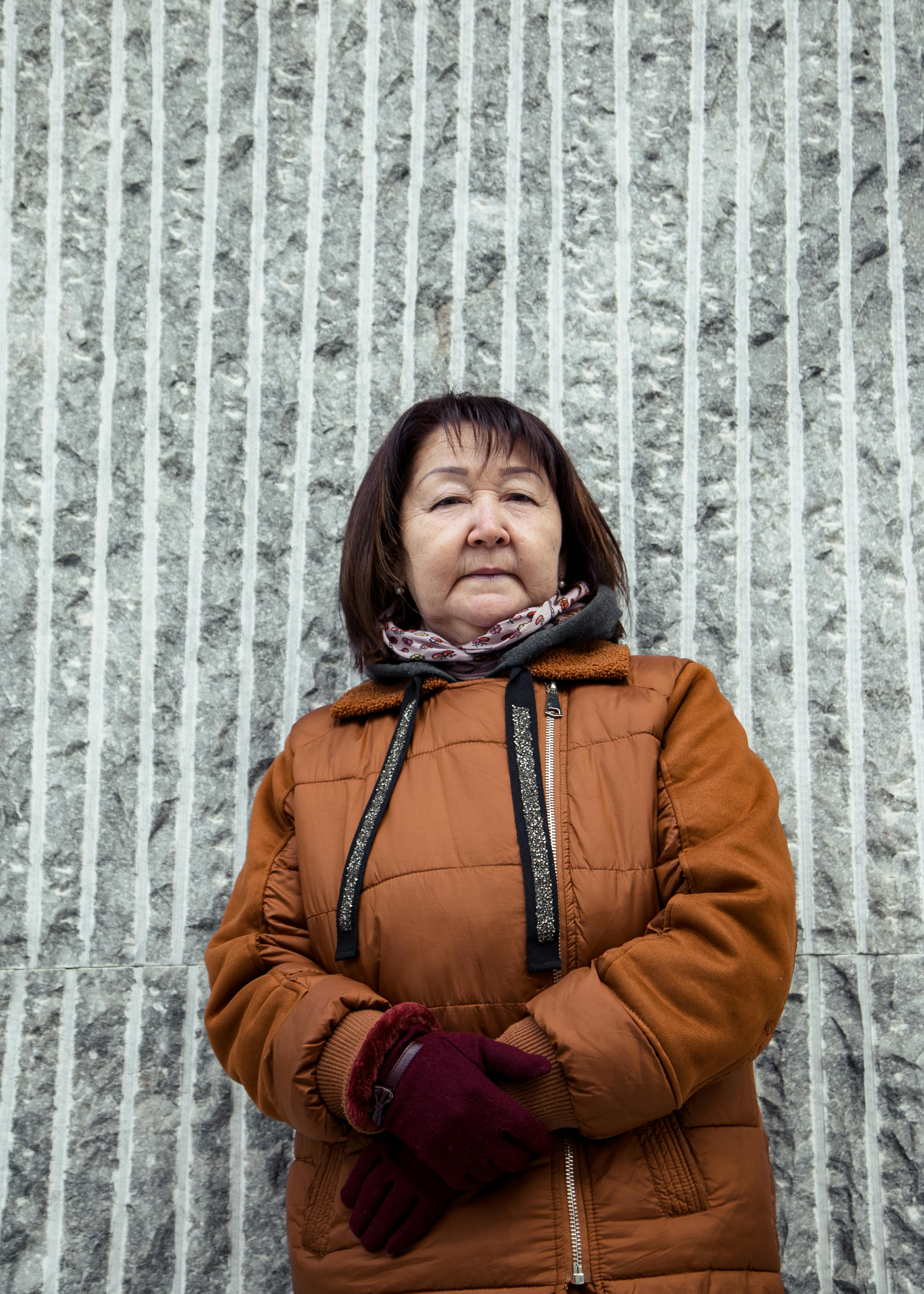 Elderly ethnic female in purple warm gloves and jacket looking at camera in daytime