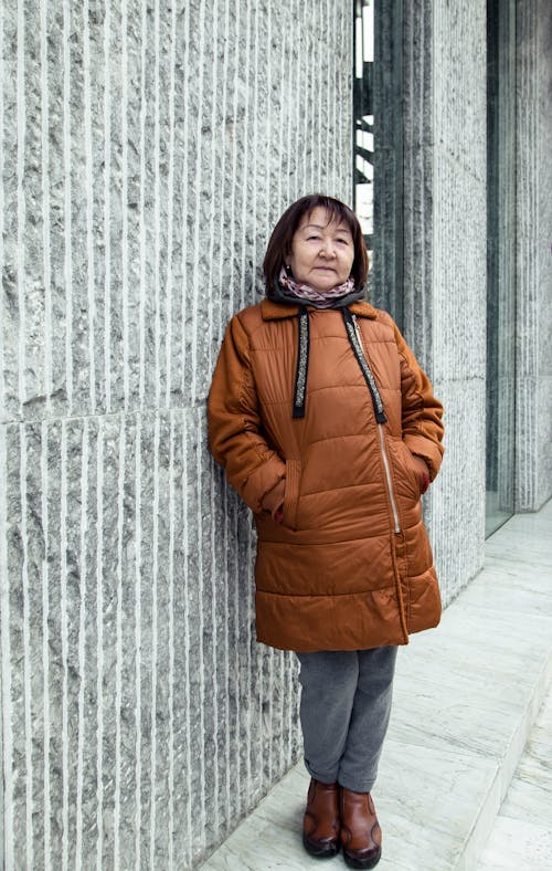 Full body of ethnic senior female looking at camera while leaning on contemporary building