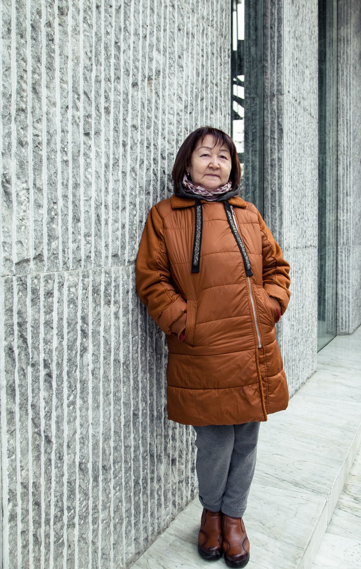 따뜻한 겨울 코트를 입고 건물 벽에 기대 선 노년 여성