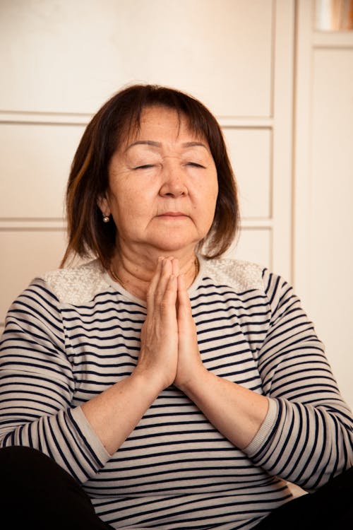 Senior Asian woman in striped sweatshirt meditating