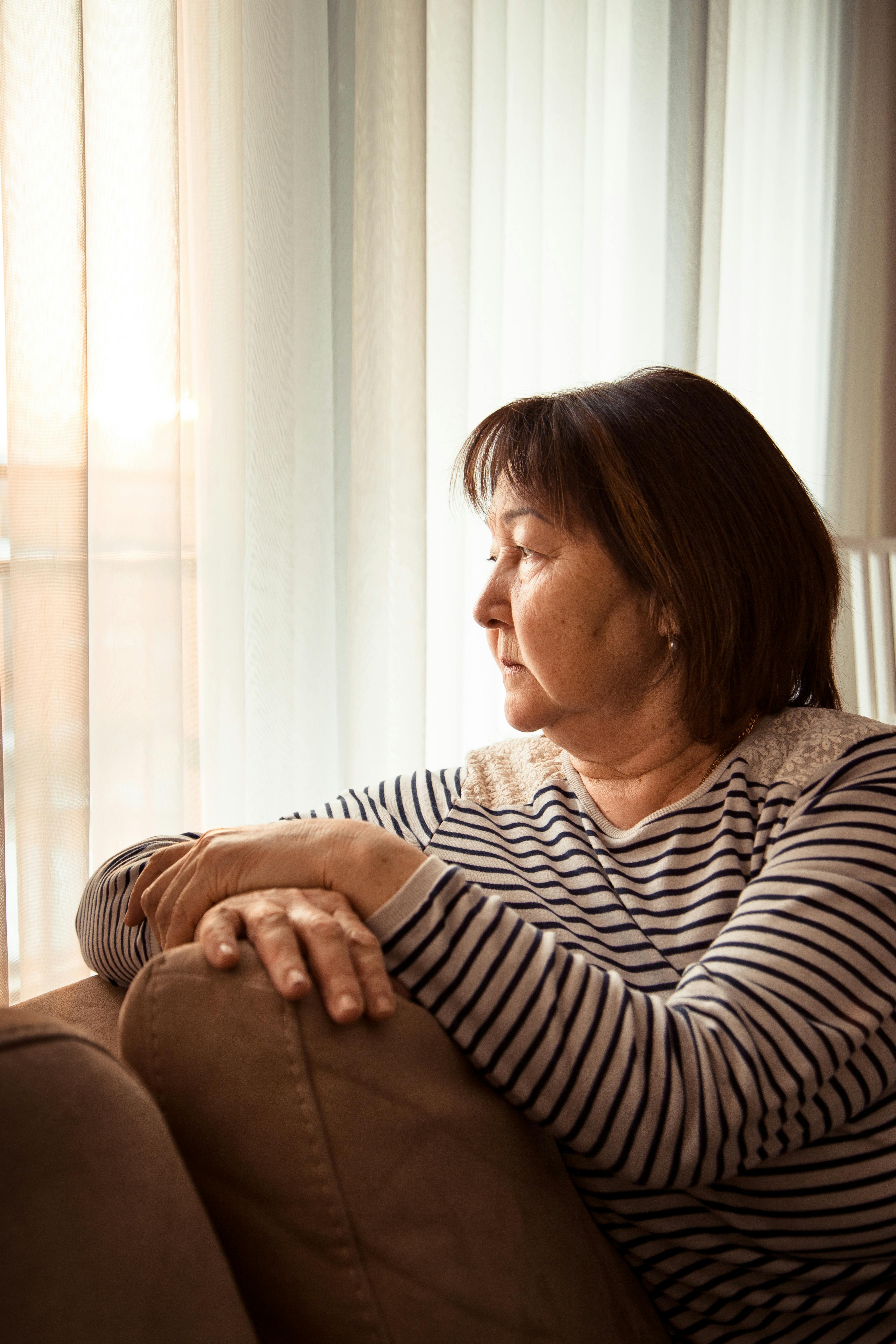 Senior Asian woman relaxing on sofa and looking in window