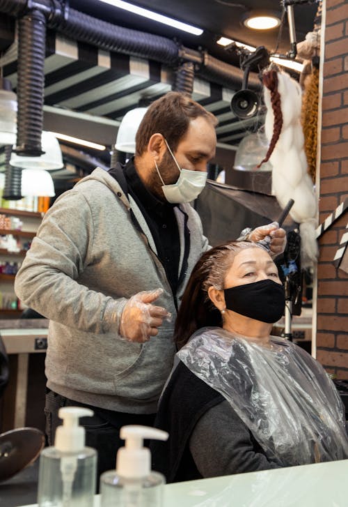 Experienced bearded hairdresser dying hair of senior woman