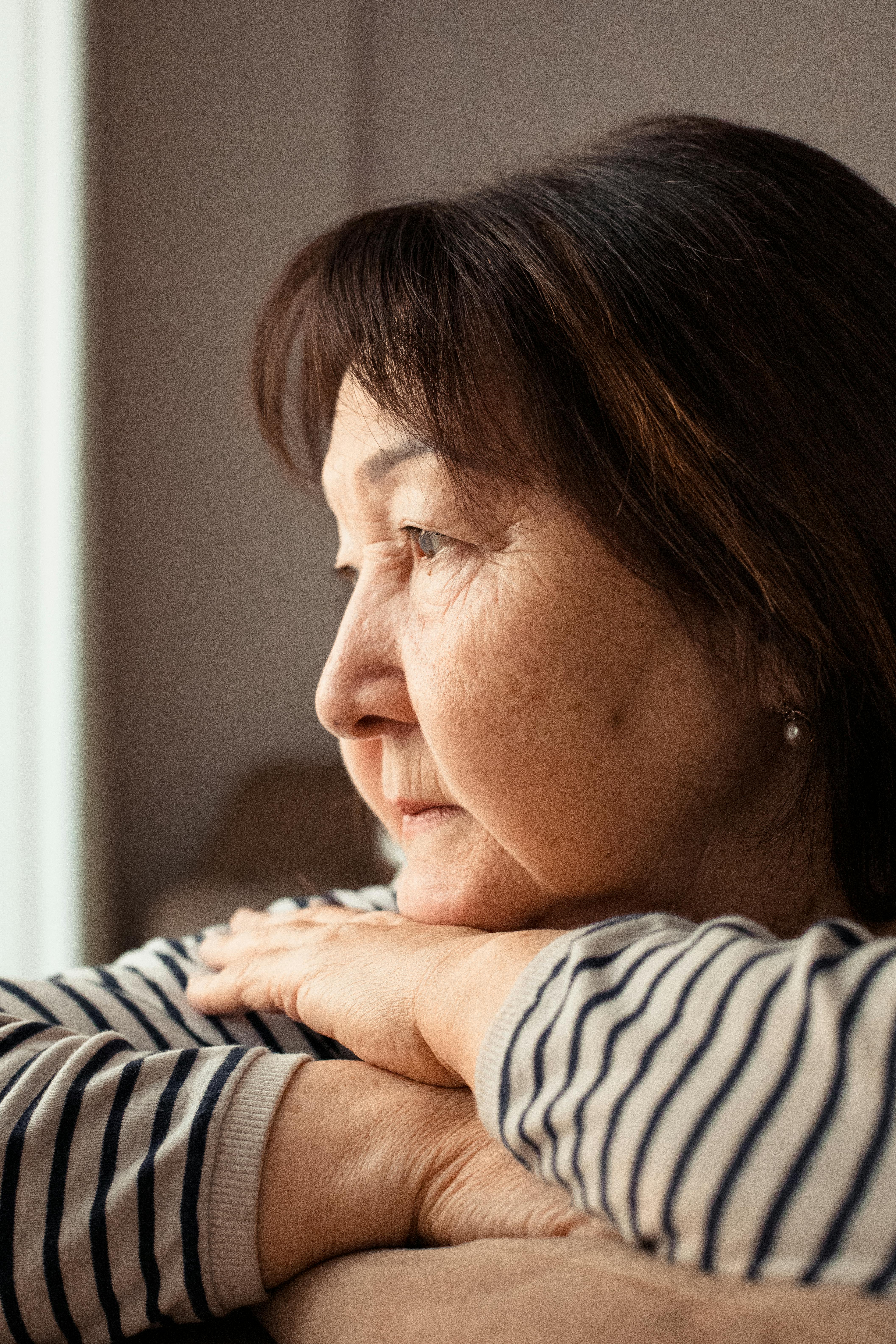 Side view of ethnic aged crop female leaning chin on hands and looking away while contemplating