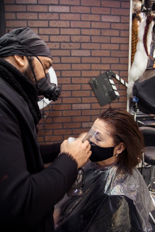 Hairstylist in respirator dying hair of aged woman in mask