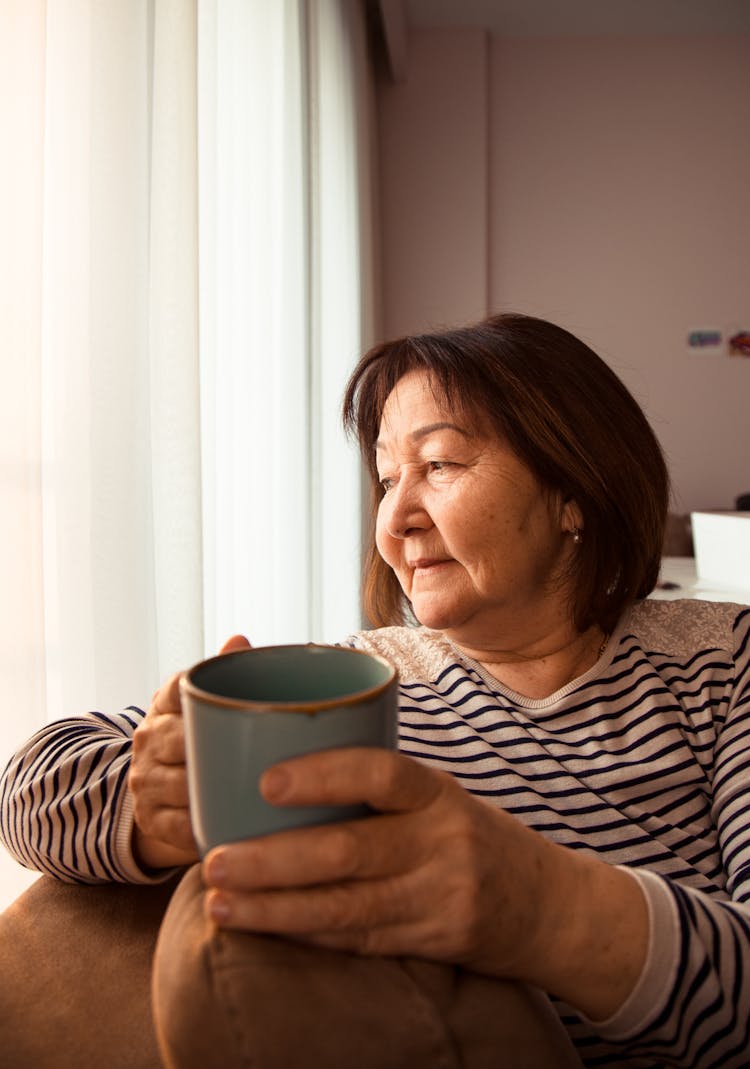 Asian Aged Woman With Cup Of Coffee Resting On Sofa