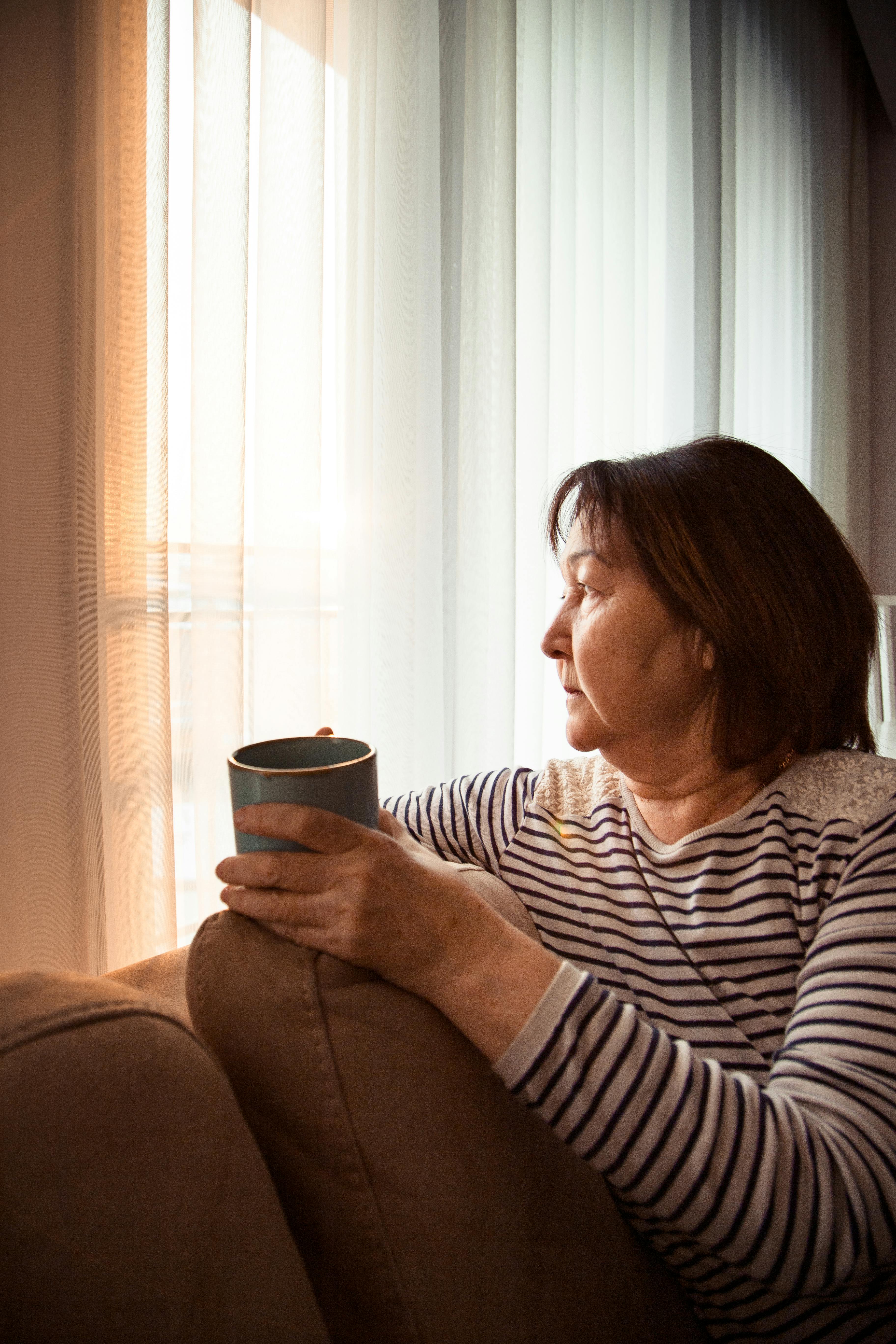 Elderly thoughtful Asian woman with cup of tea in lounge