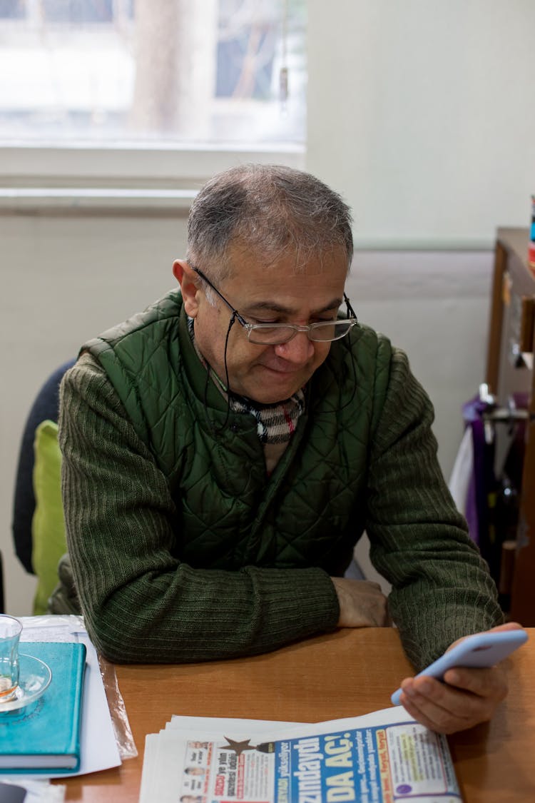 Man At Table Using Smartphone Near Newspaper In Room