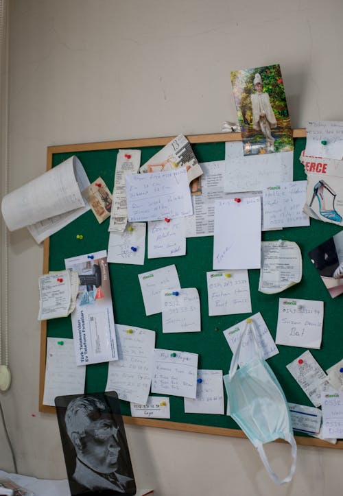 Green board with papers with written information on stationery buttons near mask and photo in light workspace