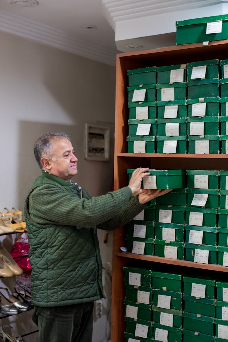 Male Seller In Shoe Store Near Shelves With Boxes