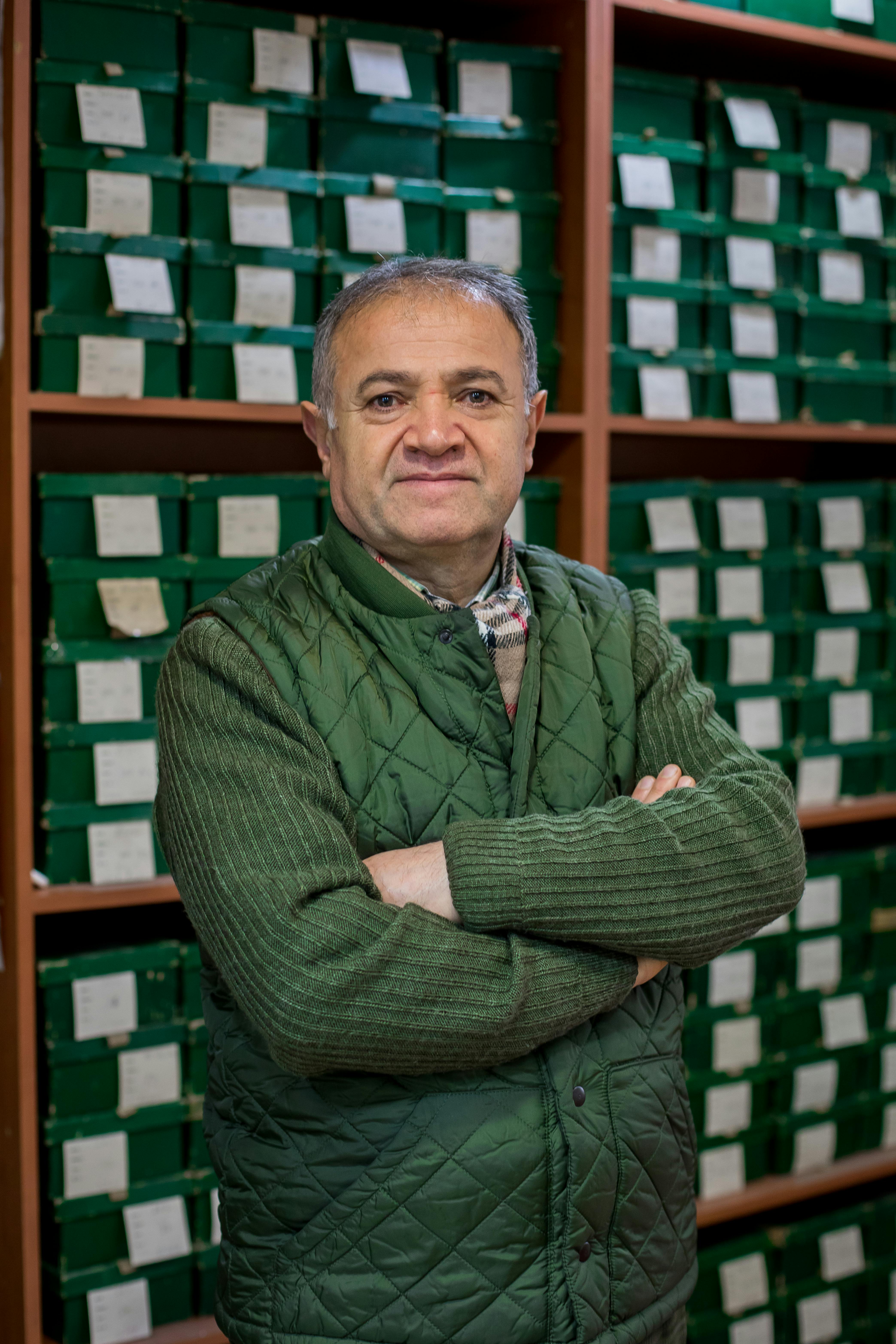 elderly man standing with crossed arms against shelves with boxes