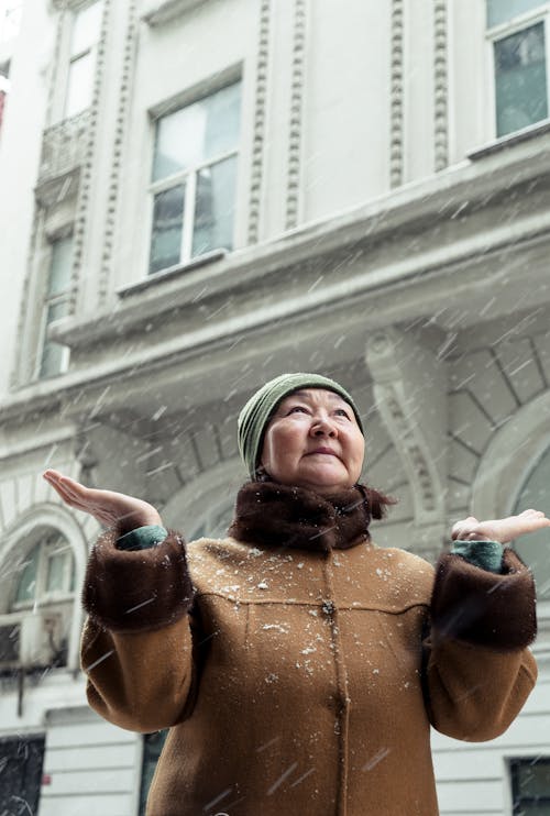 Elderly Asian woman standing on street with raised arms in snowy day