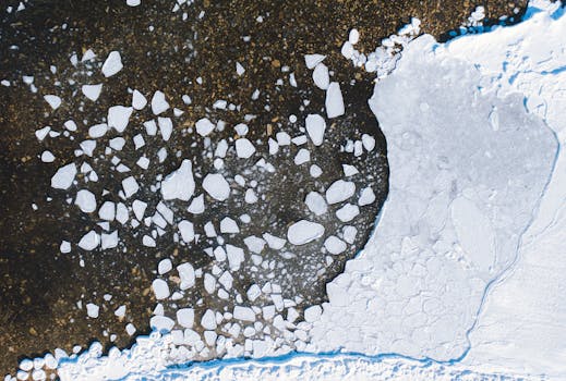 Aerial shot of ice pieces scattered across a dark lake, with snow and frozen water in winter.